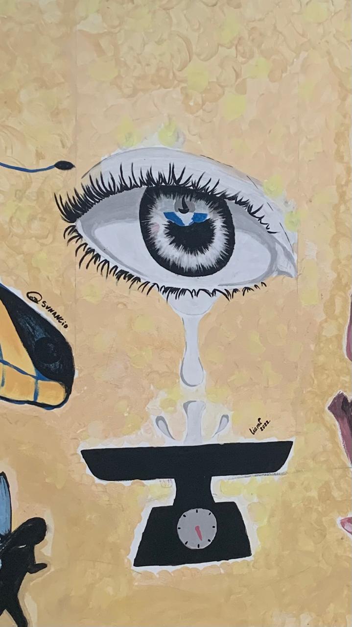 Pintura em close-up de uma parede com um fundo amarelado e pinceladas em tons de bege. O elemento central é um olho grande e estilizado com cílios longos e pretos. A íris do olho é preta, e dentro dela há um reflexo azul-claro com a silhueta de uma lua crescente, evocando o céu noturno. Uma lágrima branca cai do olho, pingando sobre uma balança preta com um mostrador rosa-claro.