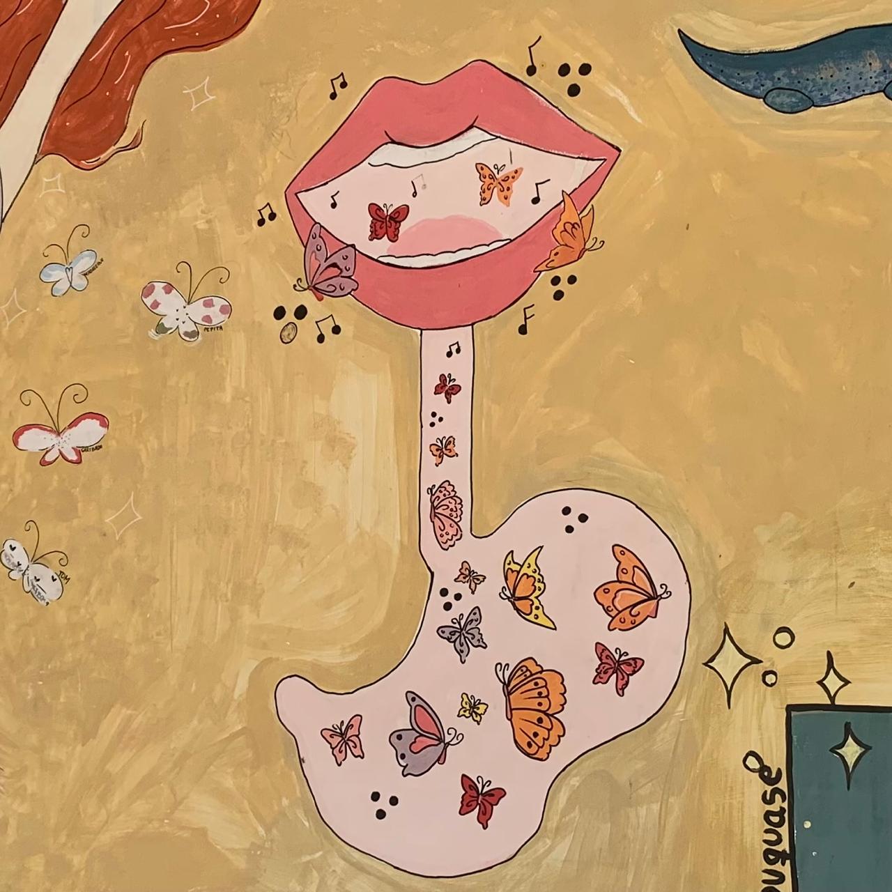 Pintura em uma parede com fundo em tons de amarelo e bege. A imagem central é uma representação surrealista de um sistema digestivo. Uma boca com lábios rosados está aberta, contendo pequenas borboletas e notas musicais. Da boca estende-se um esôfago estilizado que leva a um estômago de cor rosa claro. O estômago também está preenchido com uma variedade de borboletas de tamanhos e cores diferentes, juntamente com notas musicais. Há borboletas flutuando e brilhos ao redor da composição.