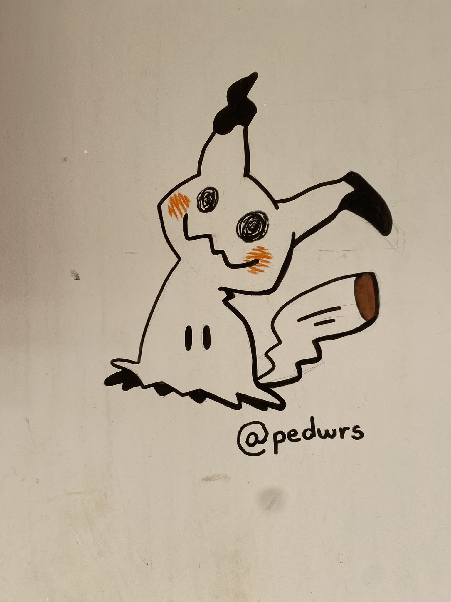 Desenho simples e estilizado do personagem Pikachu, feito com caneta preta e toques de cor em uma parede branca. O personagem tem um corpo esvoaçante de cor clara, com um contorno serrilhado na base. As orelhas e a ponta da cauda (que é marrom na ponta) são escuras, e o rosto desenhado no "disfarce" tem olhos pretos e bochechas alaranjadas, evocando a aparência de um Pikachu.