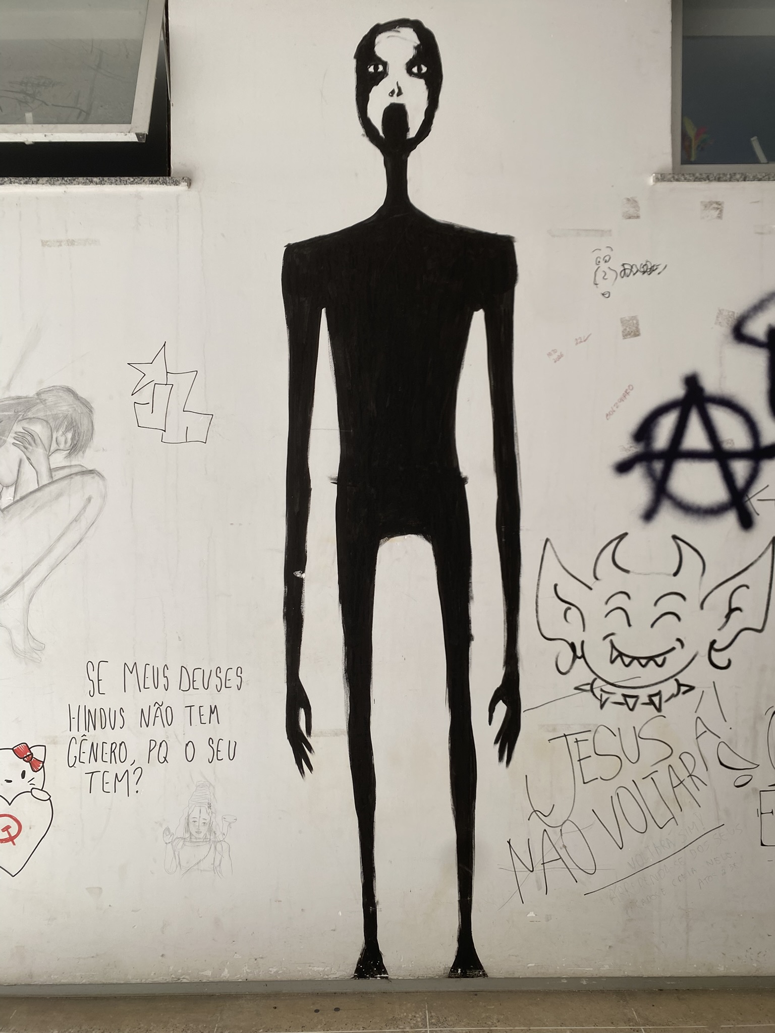 Mural em uma parede branca com janelas escuras na parte superior. O elemento central é uma figura alta e esguia, em silhueta preta, com braços e pernas longos e finos. O rosto, em destaque em branco, tem olhos grandes e vazios e a boca aberta em um grito. O corpo contrasta fortemente com o fundo.