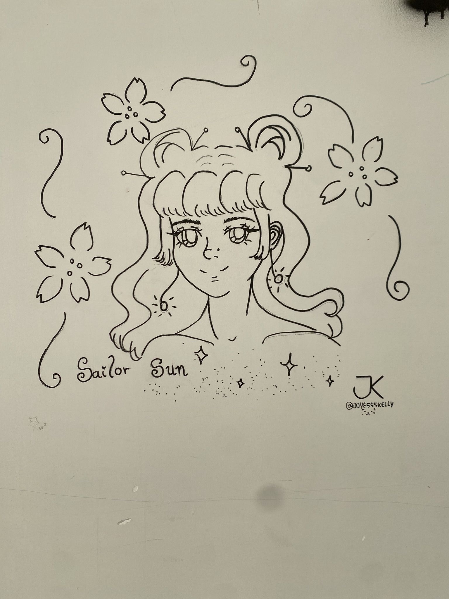A imagem apresenta um desenho em estilo mangá feito com traços pretos sobre uma superfície branca. A ilustração retrata o busto de uma personagem feminina com olhos grandes e expressivos, franja reta e um penteado com dois coques no topo da cabeça, lembrando a Sailor Moon. Ela está cercada por flores de cerejeira estilizadas, linhas curvas e pequenos brilhos em formato de estrelas, acompanhada pelo texto "Sailor Sun" e uma assinatura com as iniciais "JK" e o usuário "@JOYCE555KELLY" no canto inferior direito.