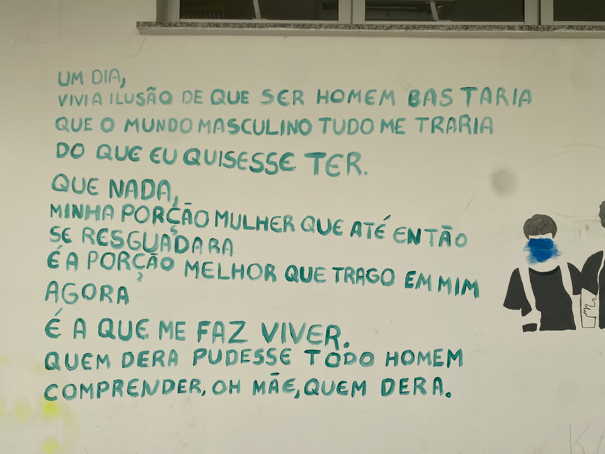 A imagem apresenta um longo texto poético pintado numa parede branca com letras maiúsculas em tom de verde-água, disposto à esquerda de uma pintura de duas figuras com rostos cobertos por tinta azul. O poema reflete sobre a descoberta da identidade e a expressão de gênero. O poema diz ""Um dia, vivi a ilusão de que ser homem bastaria. que o mundo era meu e que nele eu mandaria. mas o tempo passou e a vida me mostrou que dentro de mim, uma porção mulher sempre habitou e ela reclamou o seu lugar, o seu direito de ser e existir e hoje, ela é quem me faz mais viva, mais livre e mais feliz".