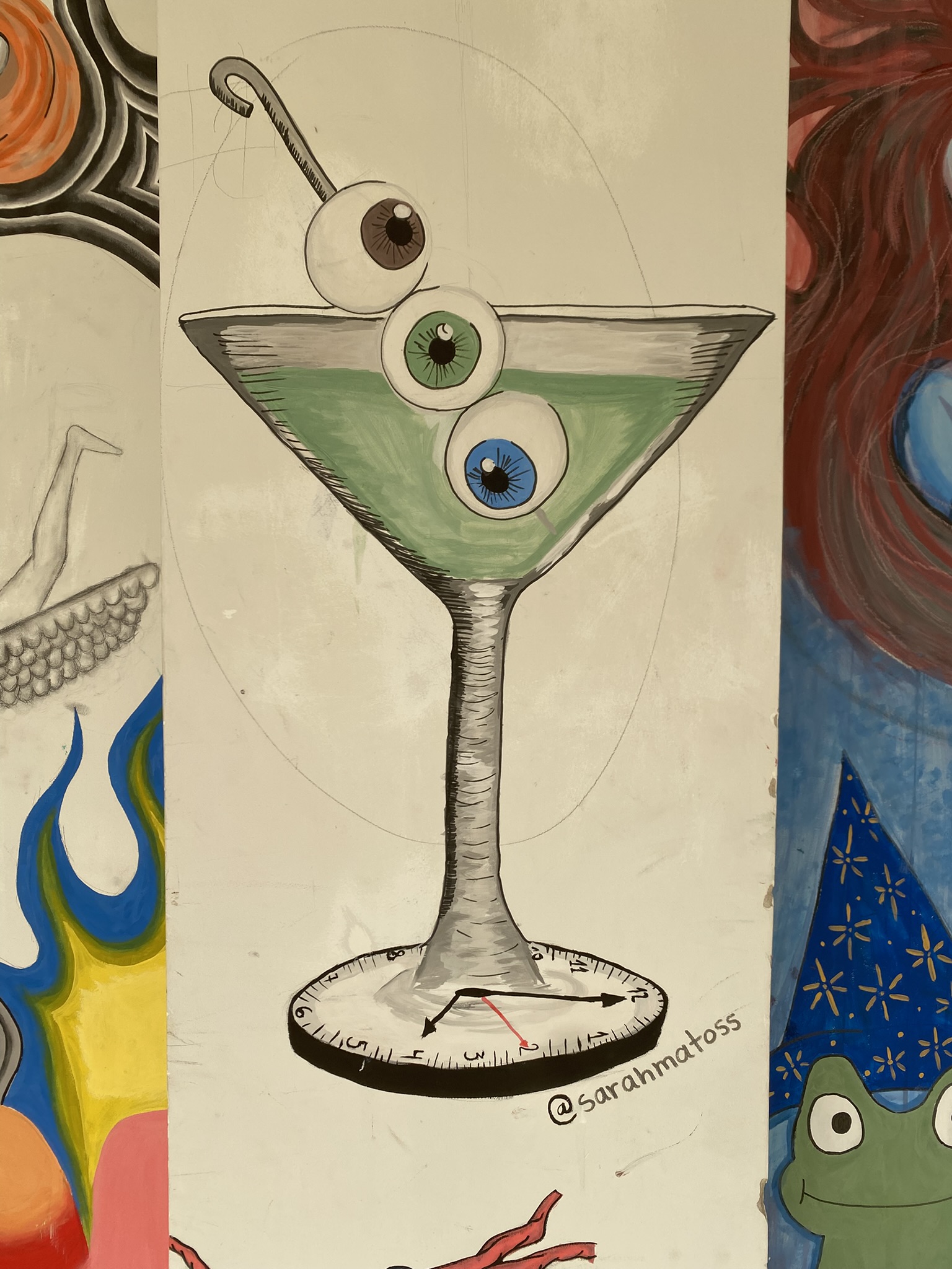 A imagem apresenta a ilustração de uma taça de Martini com um líquido verde, contendo três globos oculares (marrom, verde e azul) espetados por um palito. A base da taça é desenhada como o mostrador de um relógio com ponteiros e números.