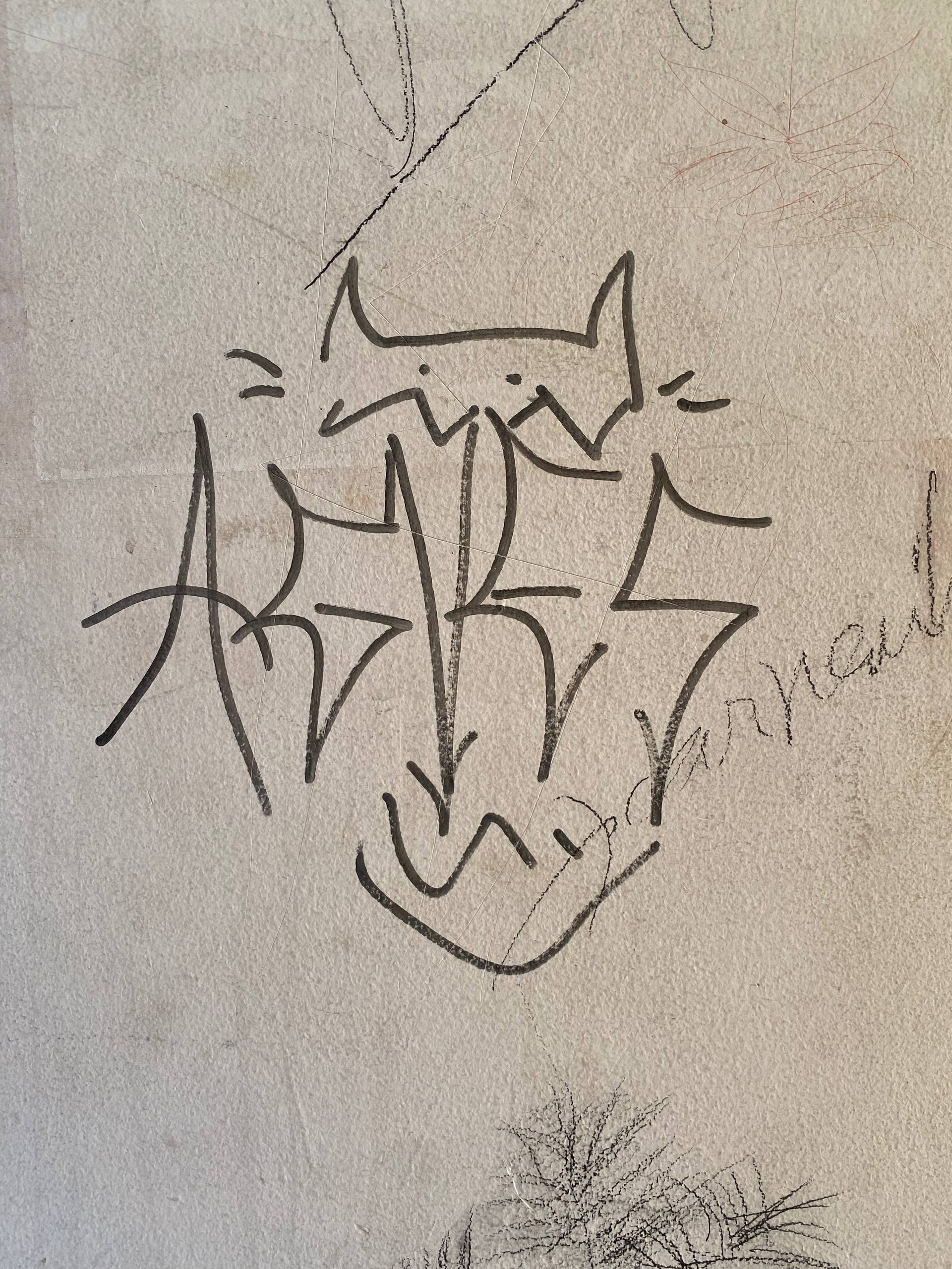 A imagem apresenta um grafite minimalista feito com traço preto sobre uma superfície clara e texturizada. O desenho estilizado assemelha-se a uma cabeça de animal com orelhas pontiagudas, fundindo-se a letras angulares que parecem formar um nome ou pseudônimo.