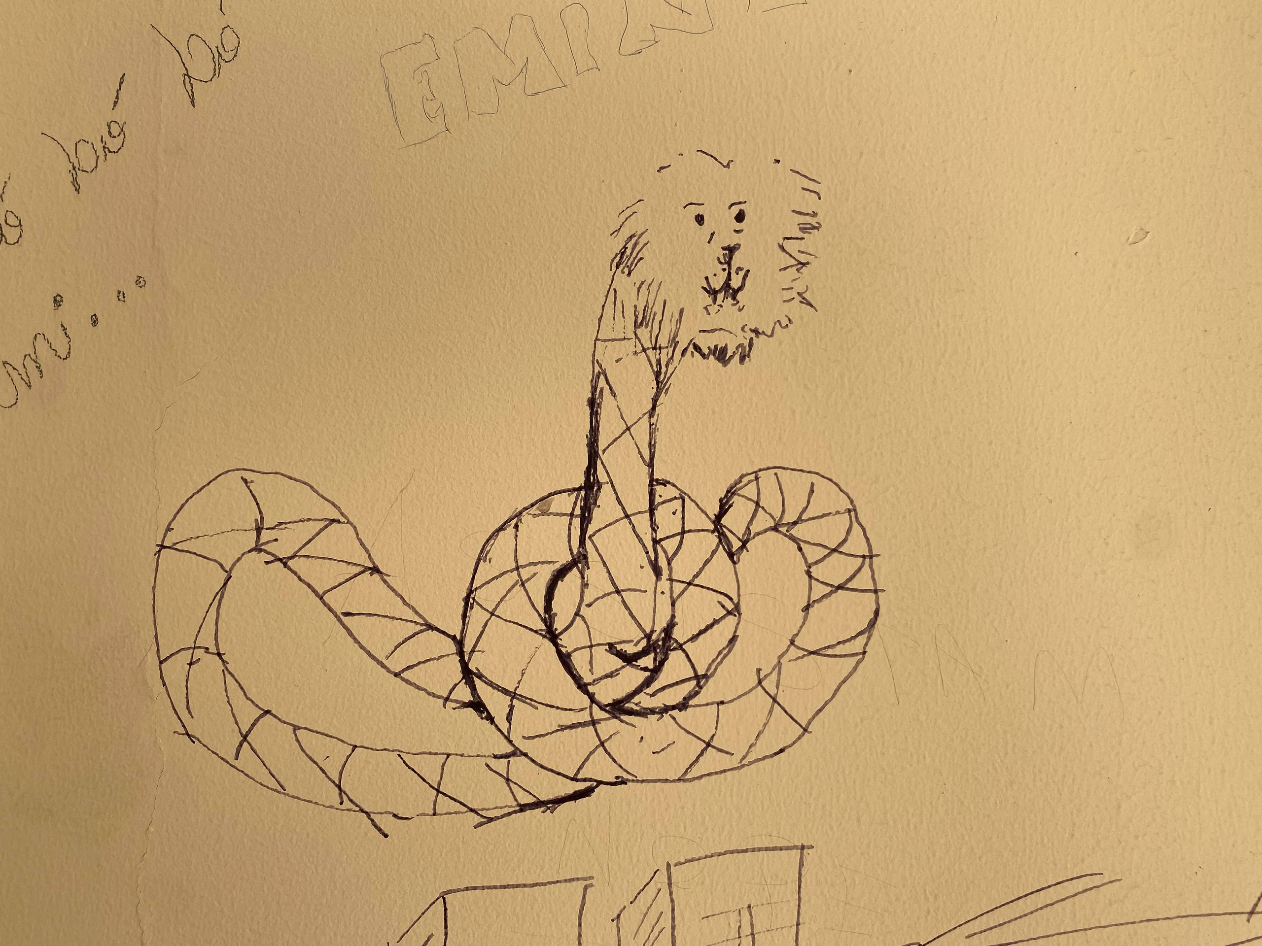 A imagem apresenta um desenho lúdico e simples feito com caneta preta sobre uma parede de tom amarelado. A ilustração retrata uma criatura híbrida, possuindo o corpo longo e enrolado de uma serpente com padrões quadriculados e a cabeça de um leão com juba e feições faciais minimalistas.