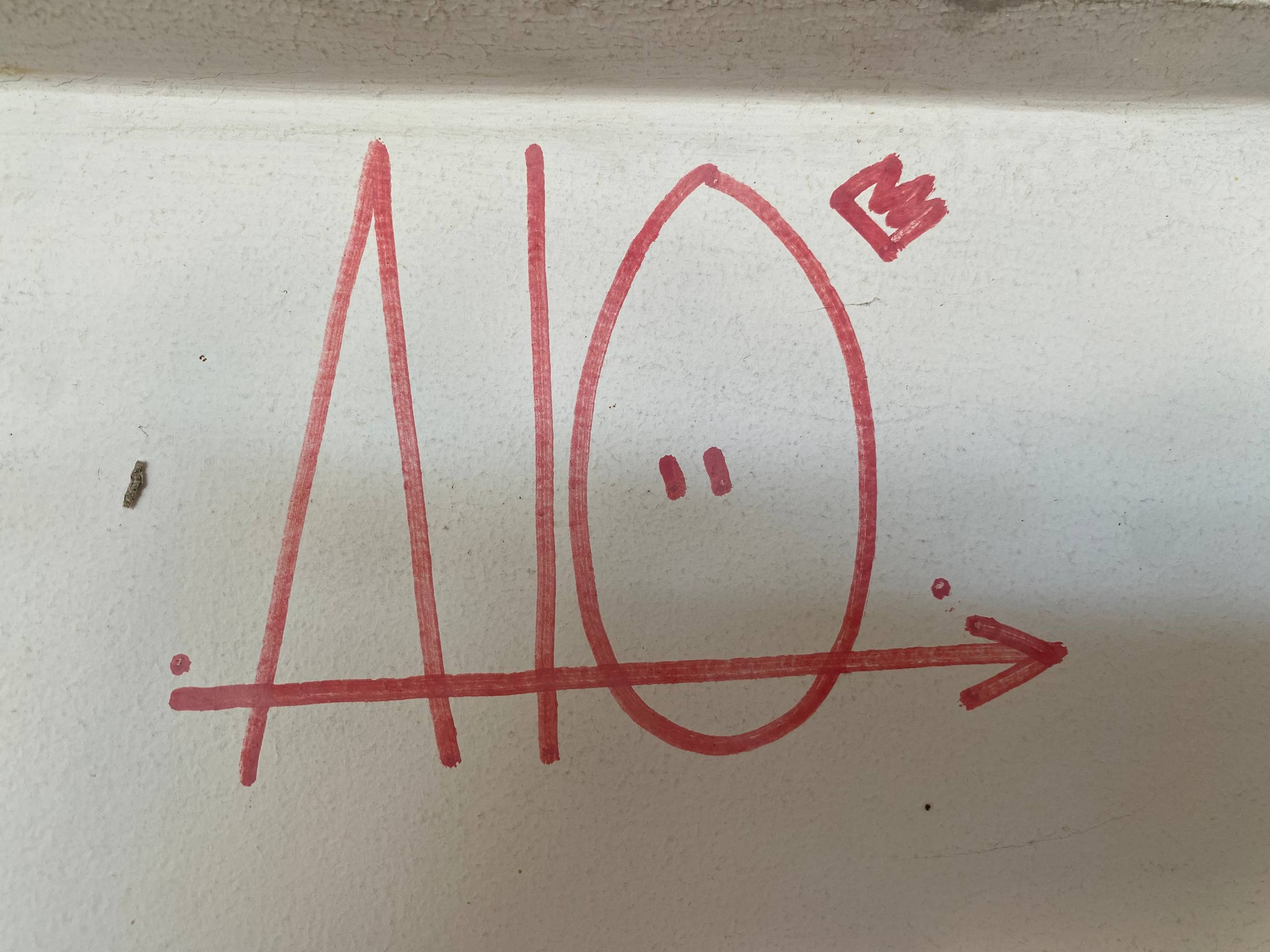 A imagem apresenta um grafite minimalista feito com marcador vermelho sobre uma superfície branca. O desenho consiste em formas geométricas e símbolos lineares: à esquerda, um triângulo alongado atravessado por uma linha horizontal; no centro, uma forma oval contendo dois pequenos pontos que lembram olhos; e à direita, uma pequena coroa estilizada flutuando acima da forma oval. Uma linha horizontal com uma ponta de seta na extremidade direita atravessa toda a composição, conectando os elementos.